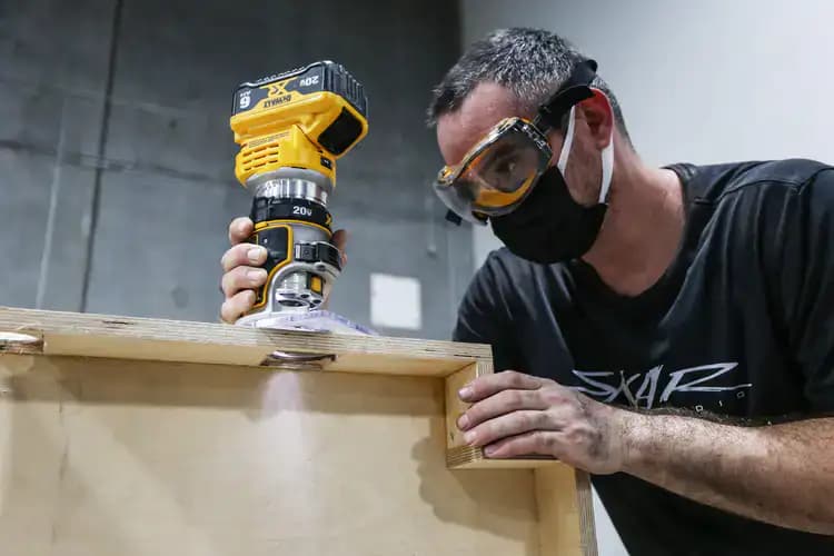 A guy holding a cordless router routing a hole in a speaker enclosure